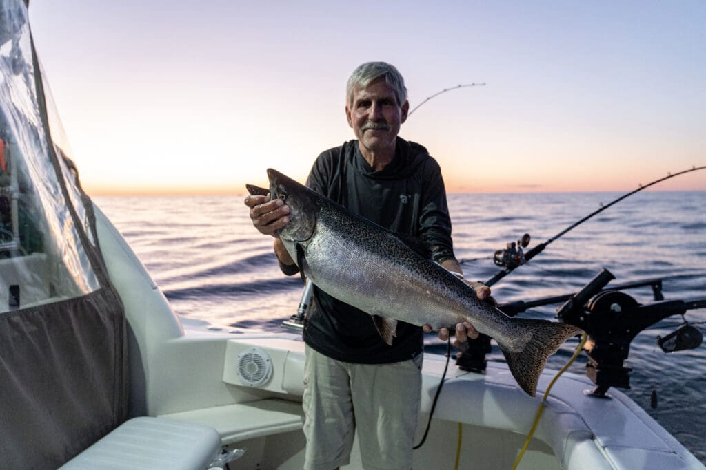 older man fishing in the ocean with fish in hand and sunset behind